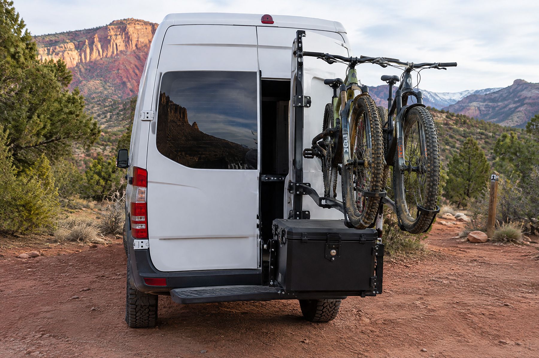 Rear-door carrier with two bikes and a box at a trailhead