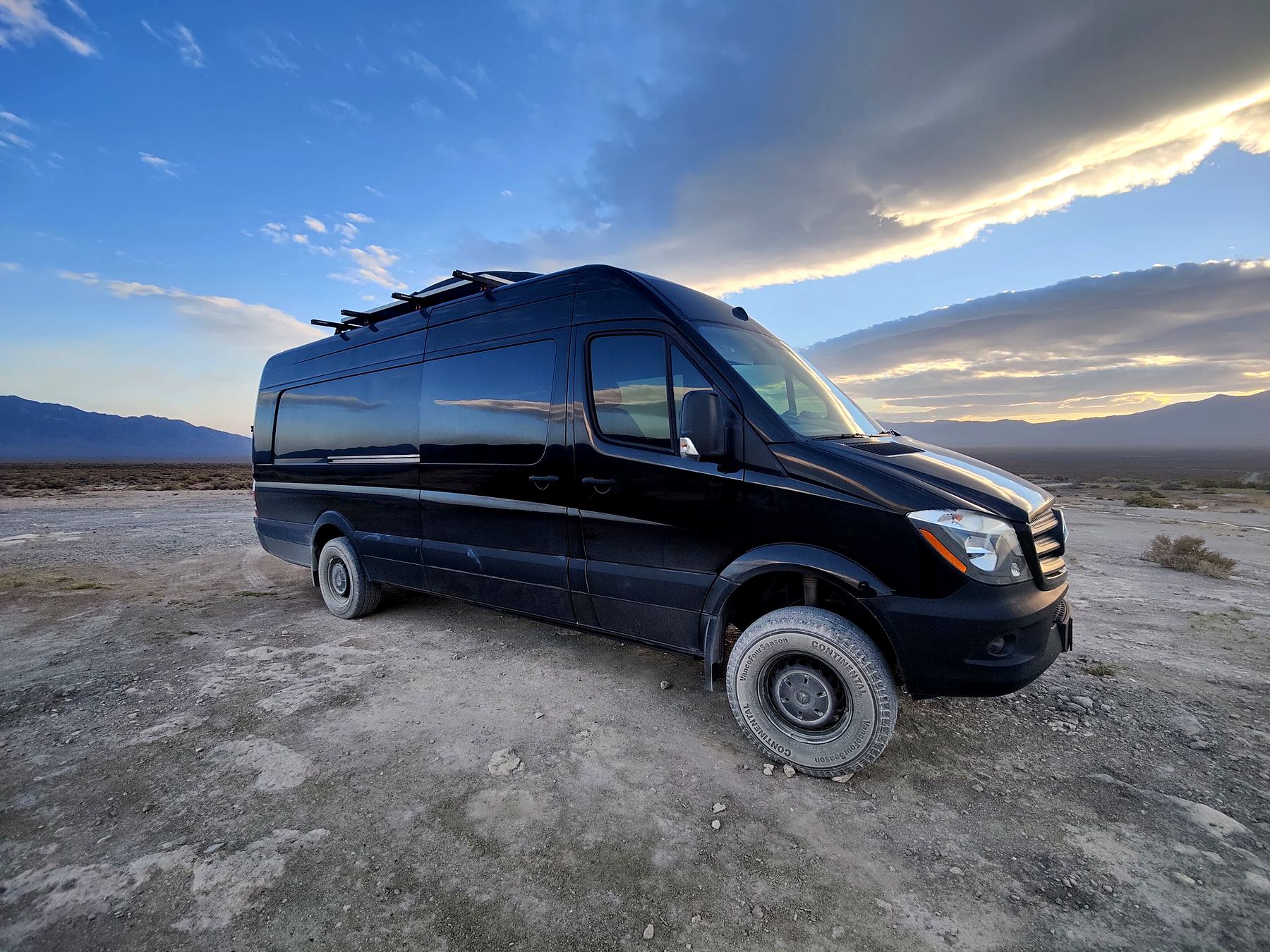 Black Sprinter with roof rack and ladder at sunset