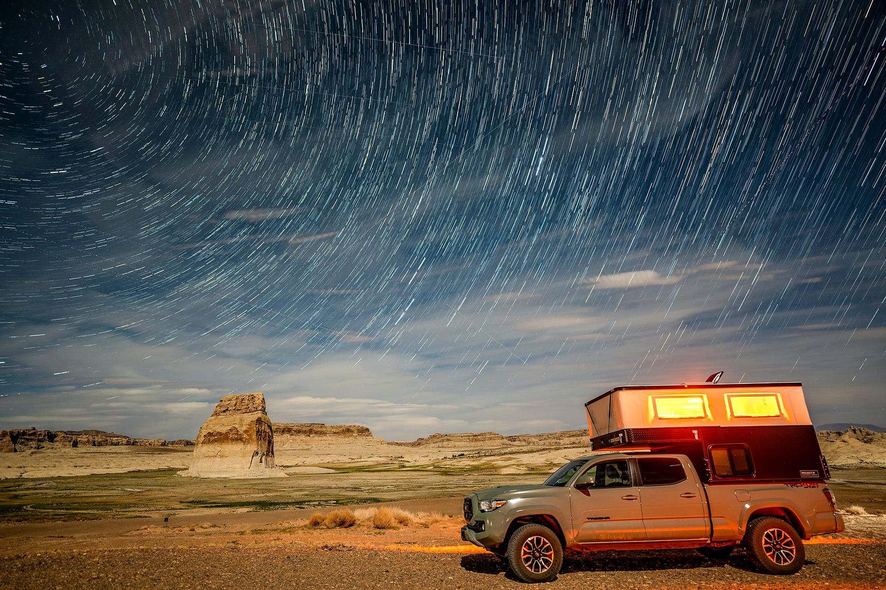 Pop-up truck camper under star trails in the desert