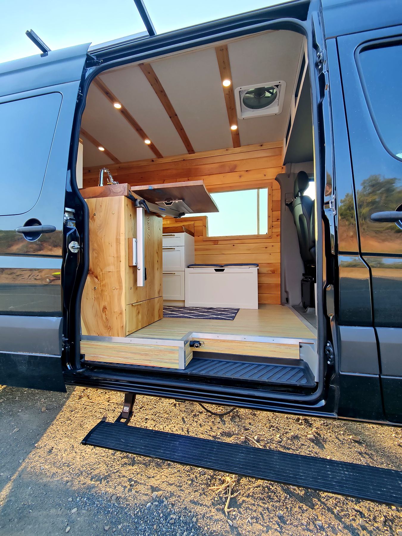Natural wood side-door galley in a black Sprinter
